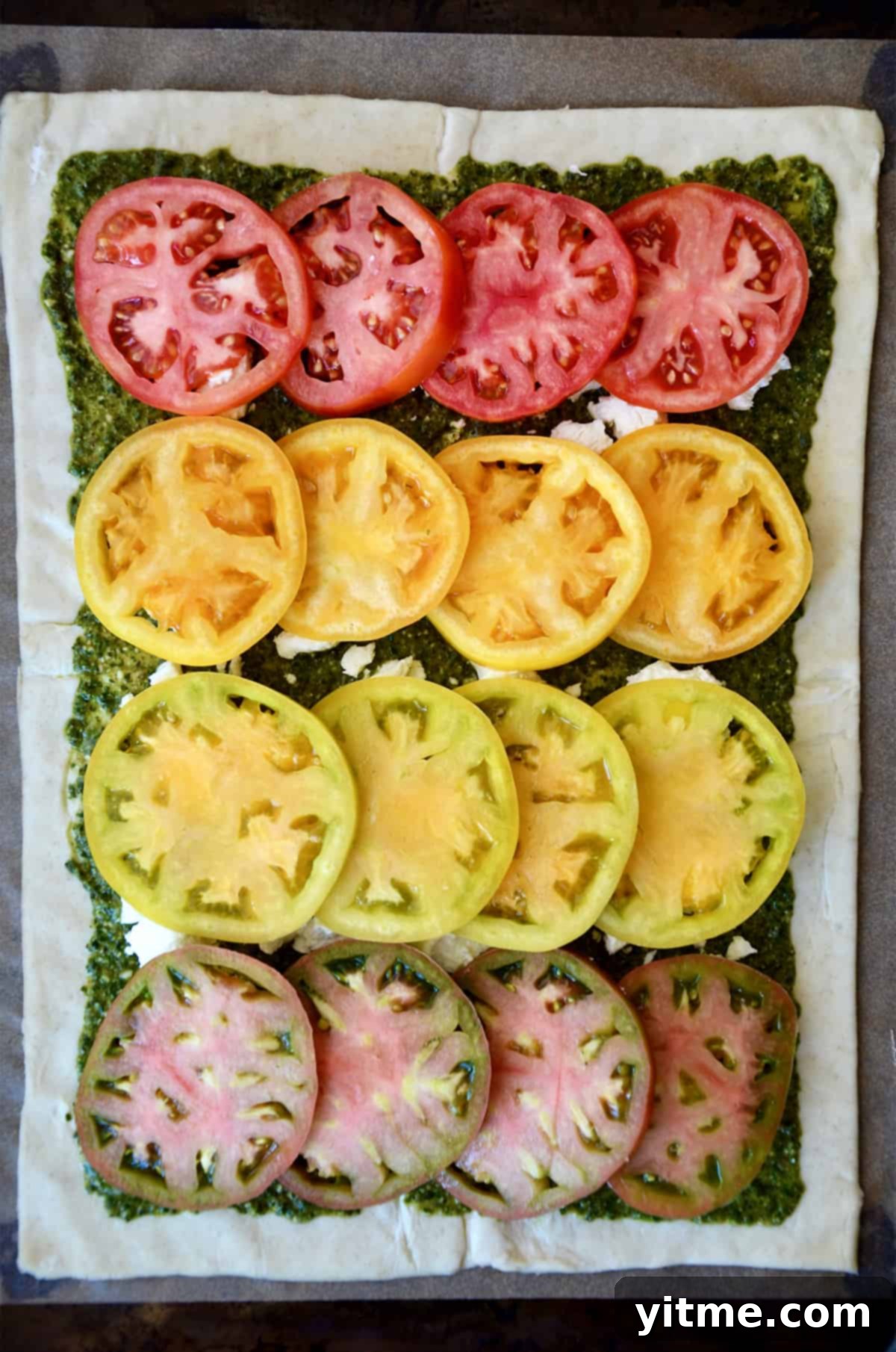 A rectangle of puff pastry topped with pesto, crumbled goat cheese, and sliced tomatoes.