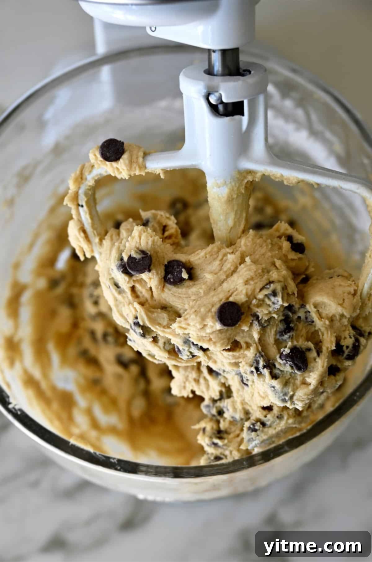 Chocolate chip cookie dough covering the paddle attachment of a stand mixer.