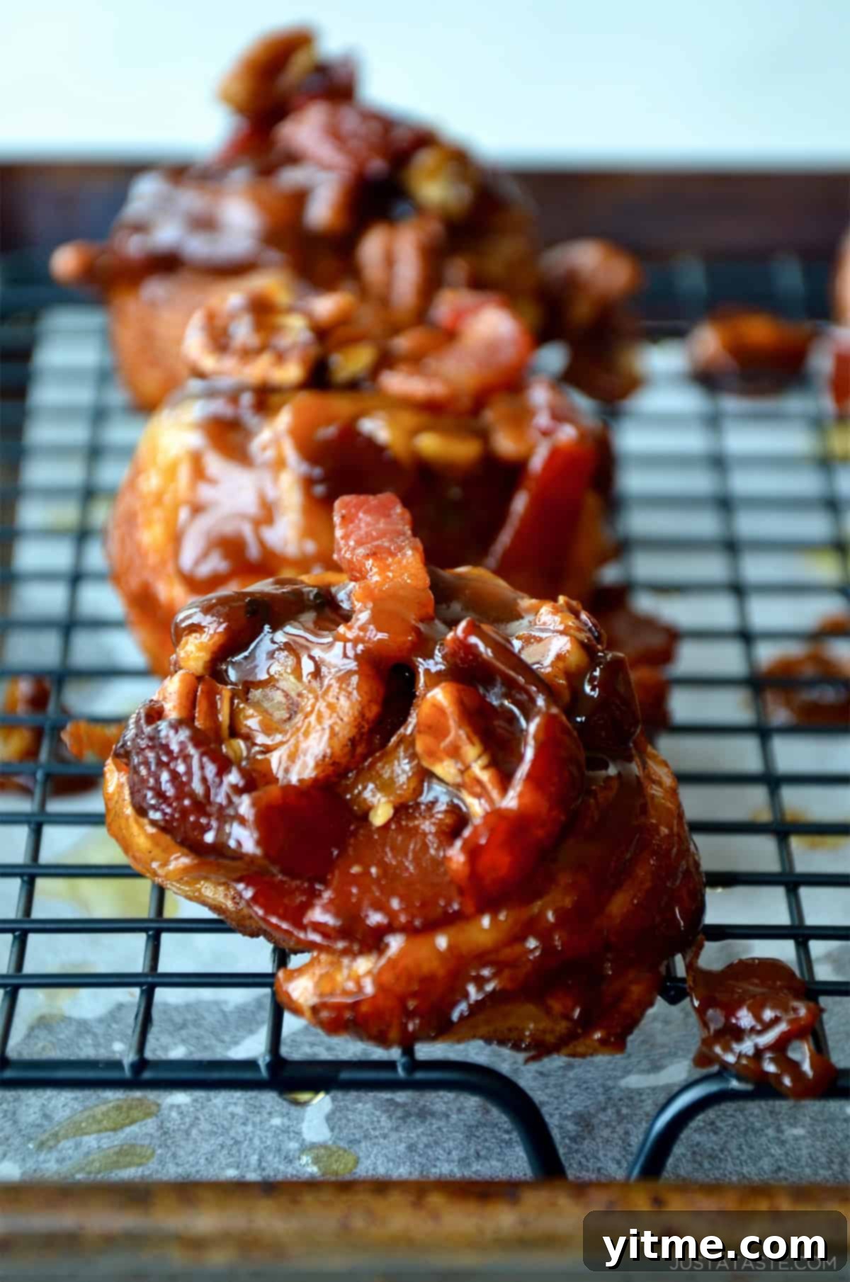Delicious sticky buns topped with bacon and pecans, cooling on a wire rack.