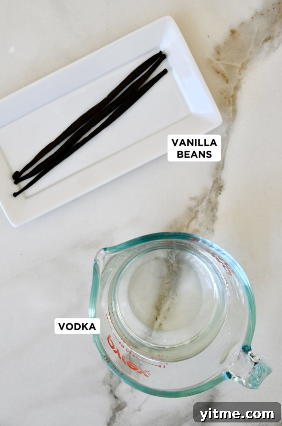Craft Your Own Vanilla Extract 3 Vanilla beans on a white plate next to a liquid measuring cup containing vodka.