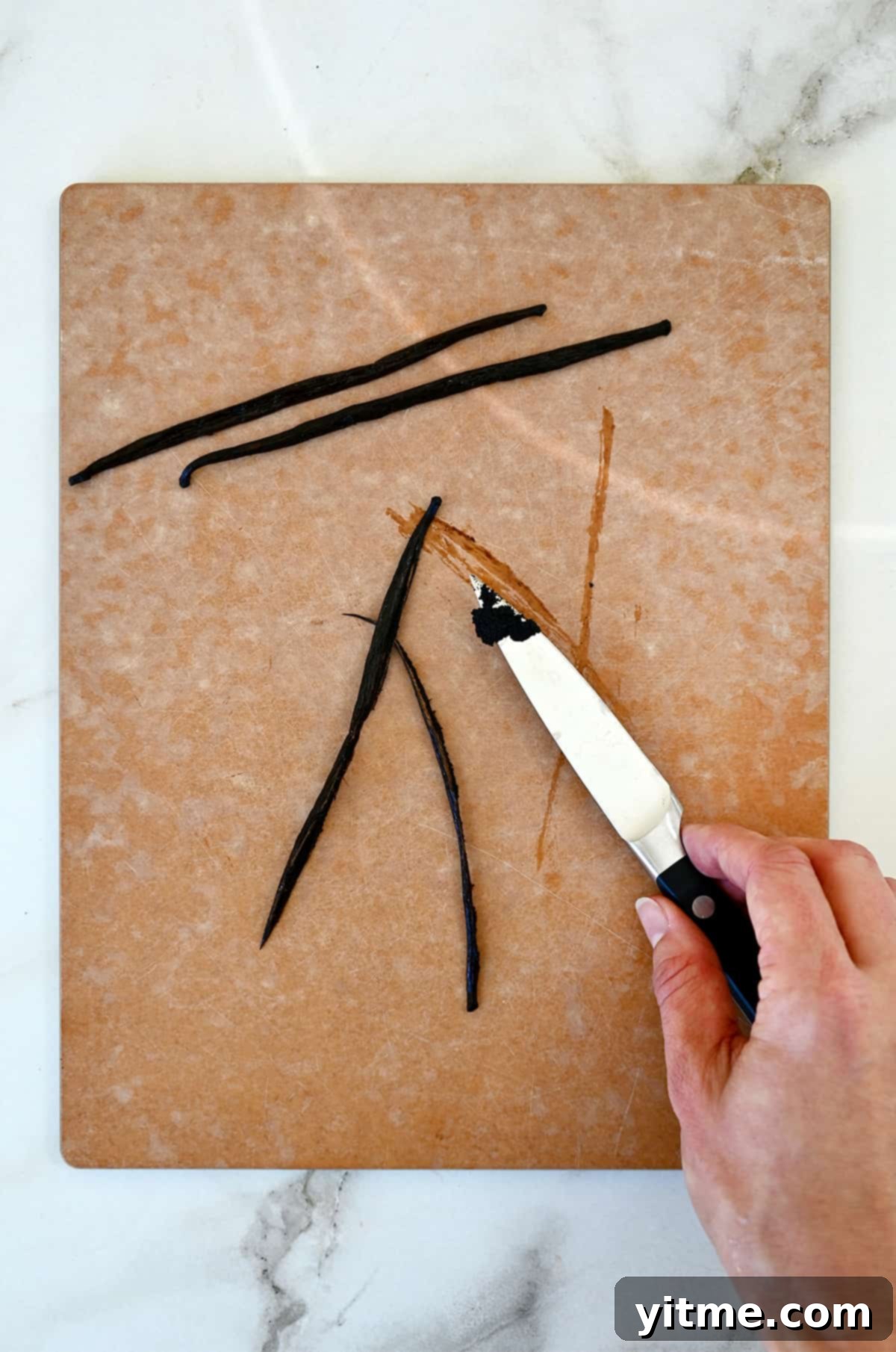 Craft Your Own Vanilla Extract 4 A hand holding a sharp knife scrapes vanilla beans out of a vanilla bean pod.