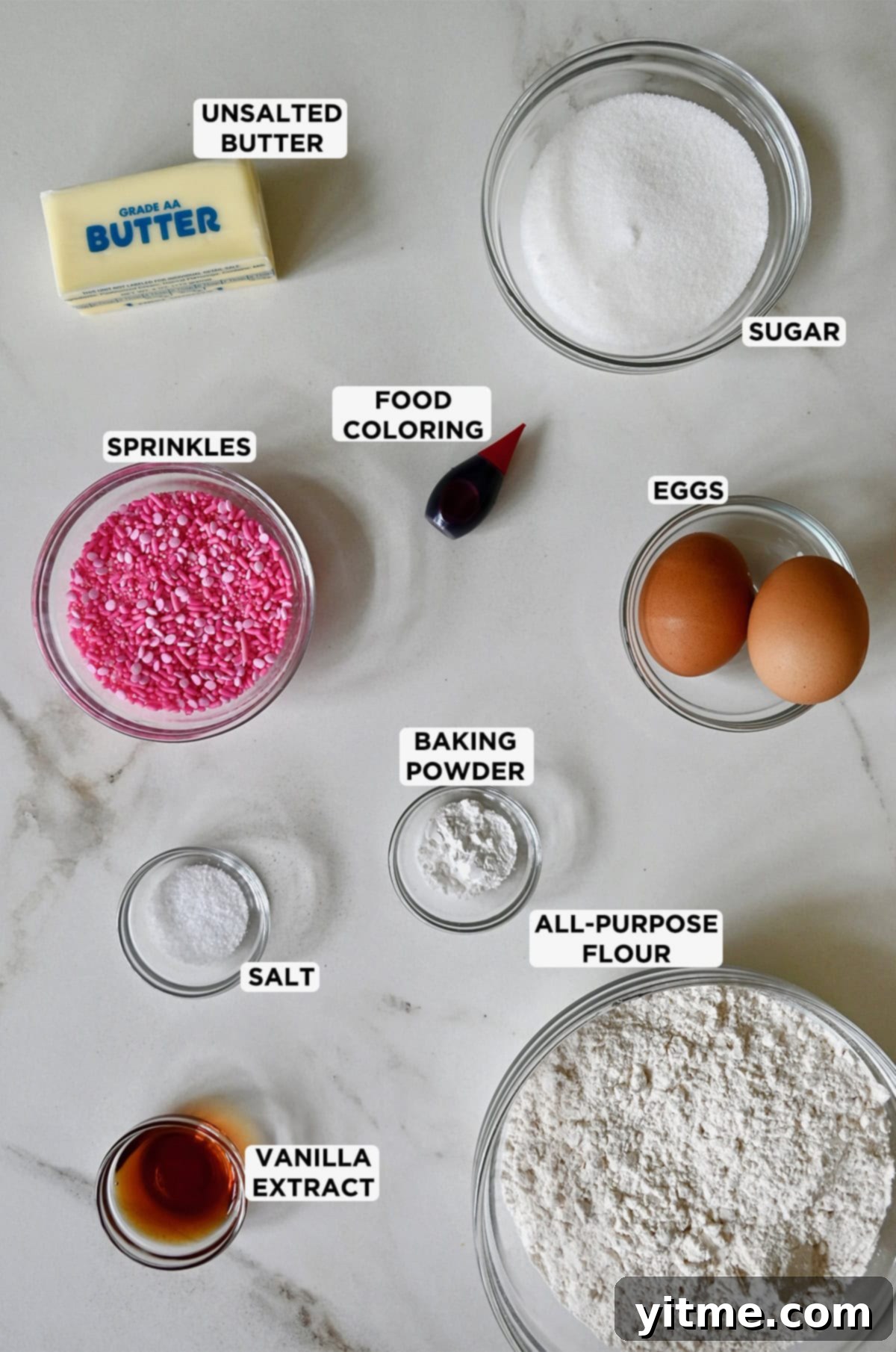 Ingredients for butter cookies are portioned into clear glass bowls, including flour, vanilla extract, salt, baking powder, eggs, sprinkles, food coloring, sugar and butter.