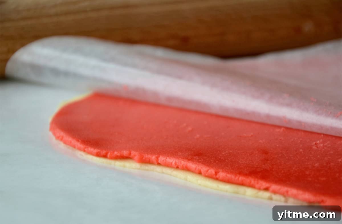 Layers of plain and pink sugar cookie dough is stacked between sheets of wax paper.