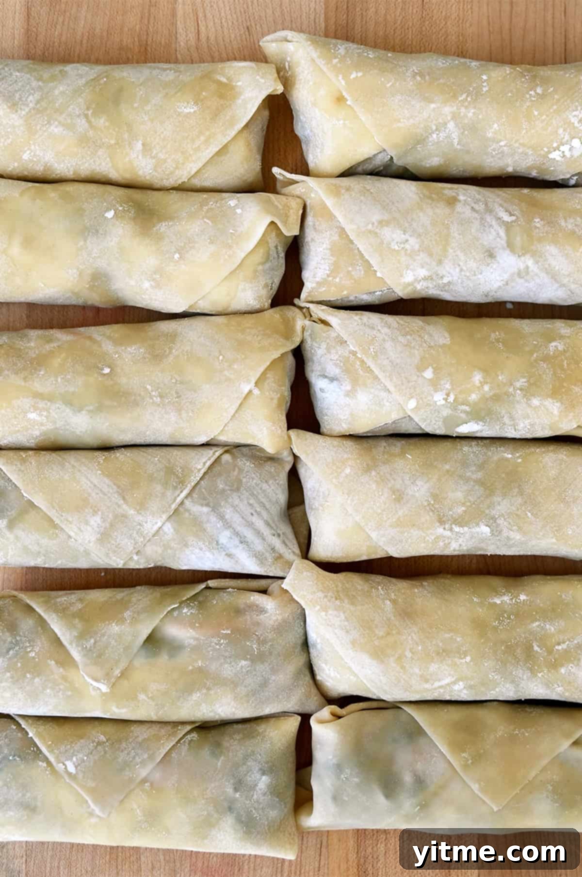 Two neat rows of perfectly rolled, uncooked pork egg rolls resting on a baking sheet, ready for frying.