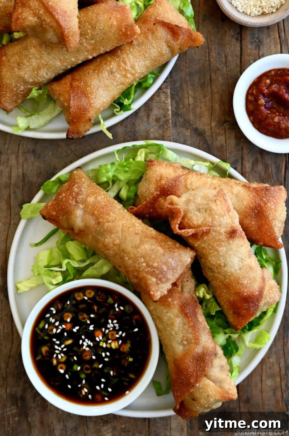 Four crispy pork egg rolls served on a bed of shredded lettuce on a white plate, accompanied by a small bowl of ginger soy dipping sauce.