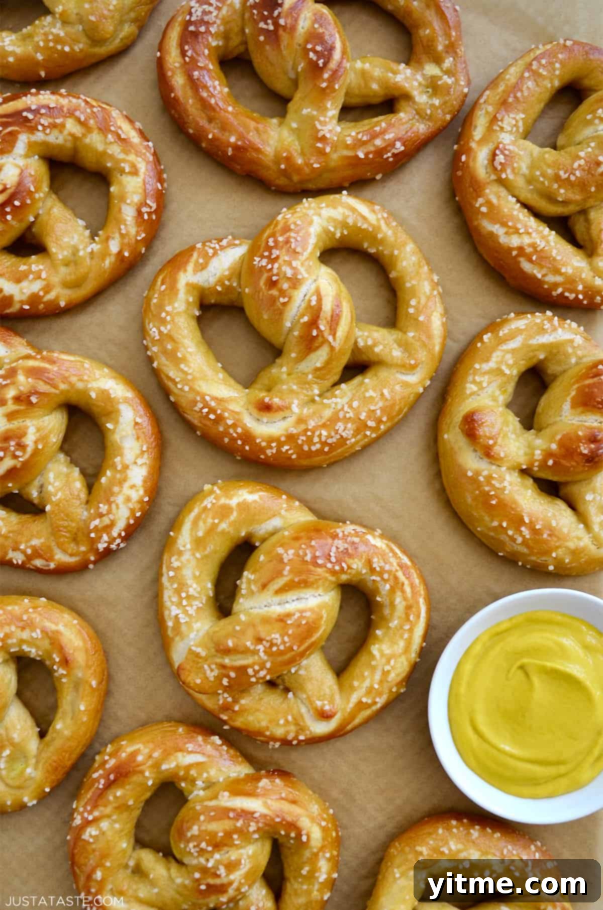 Homemade soft pretzels on brown parchment paper next to a small bowl containing yellow mustard.