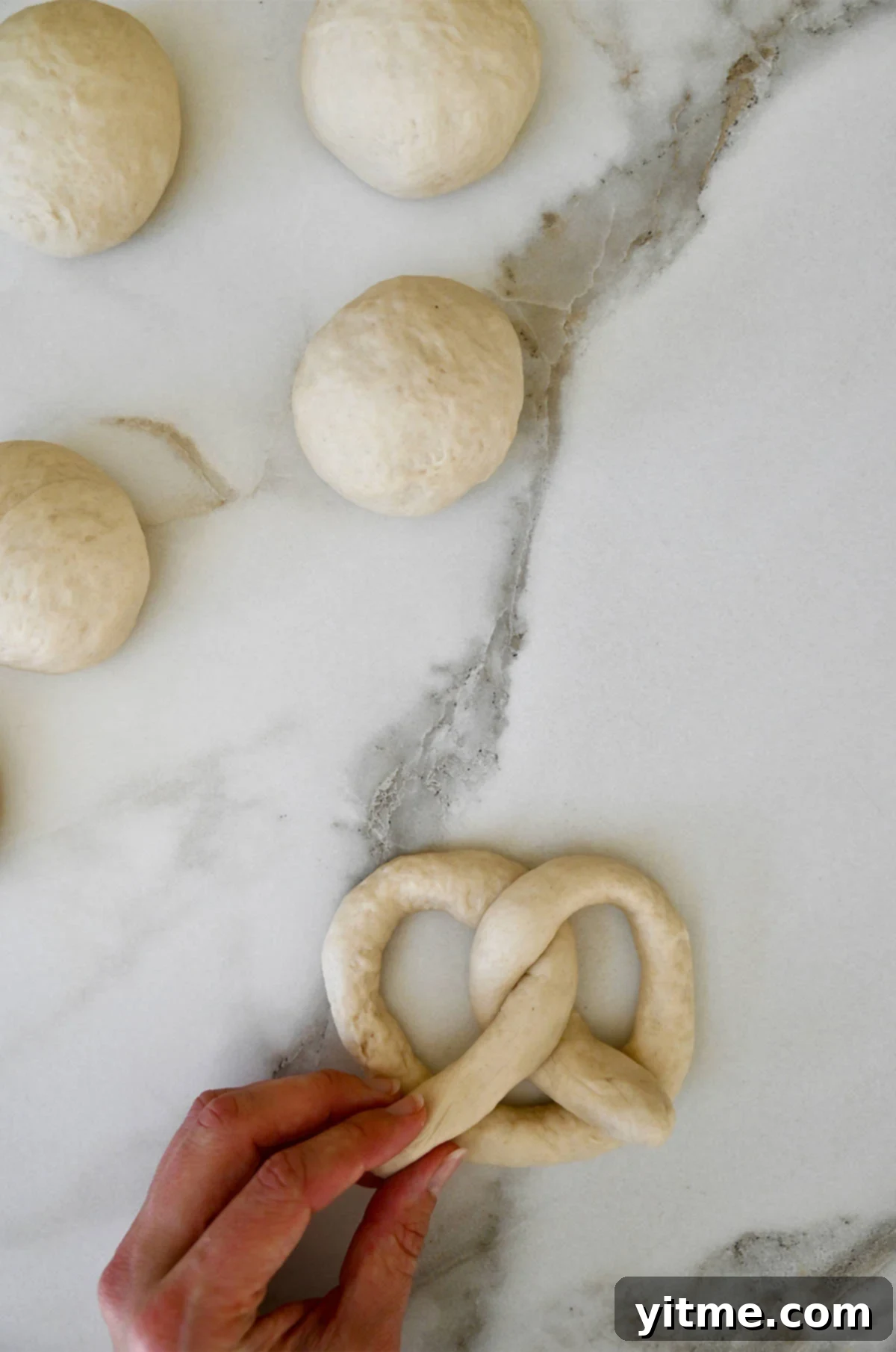 A hand twists dough into a classic pretzel shape.