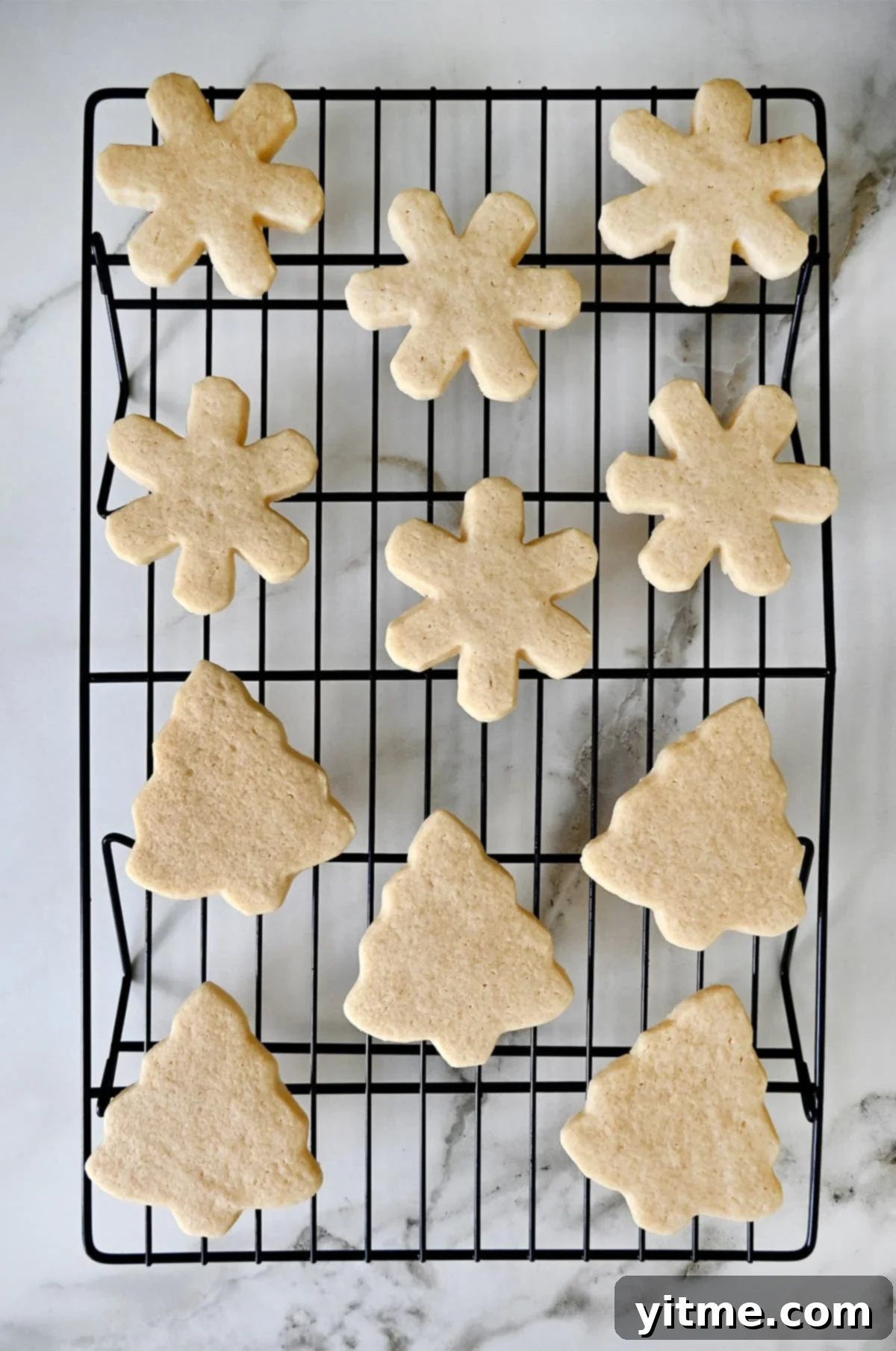 Sugar cookies in the shapes of Christmas trees and snowflakes cooling on a wire rack.