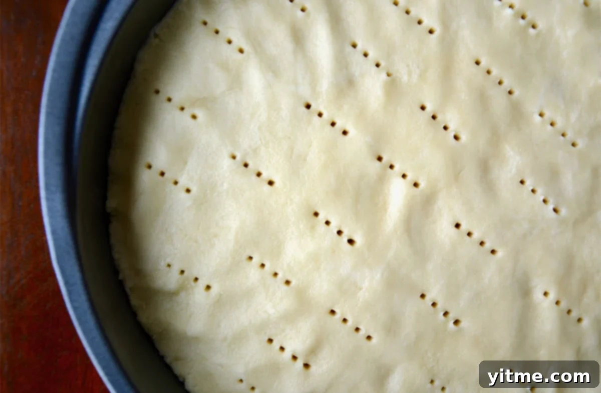 Shortbread cookie dough is pressed into a round cake pan with neat rows of prick marks from a fork.
