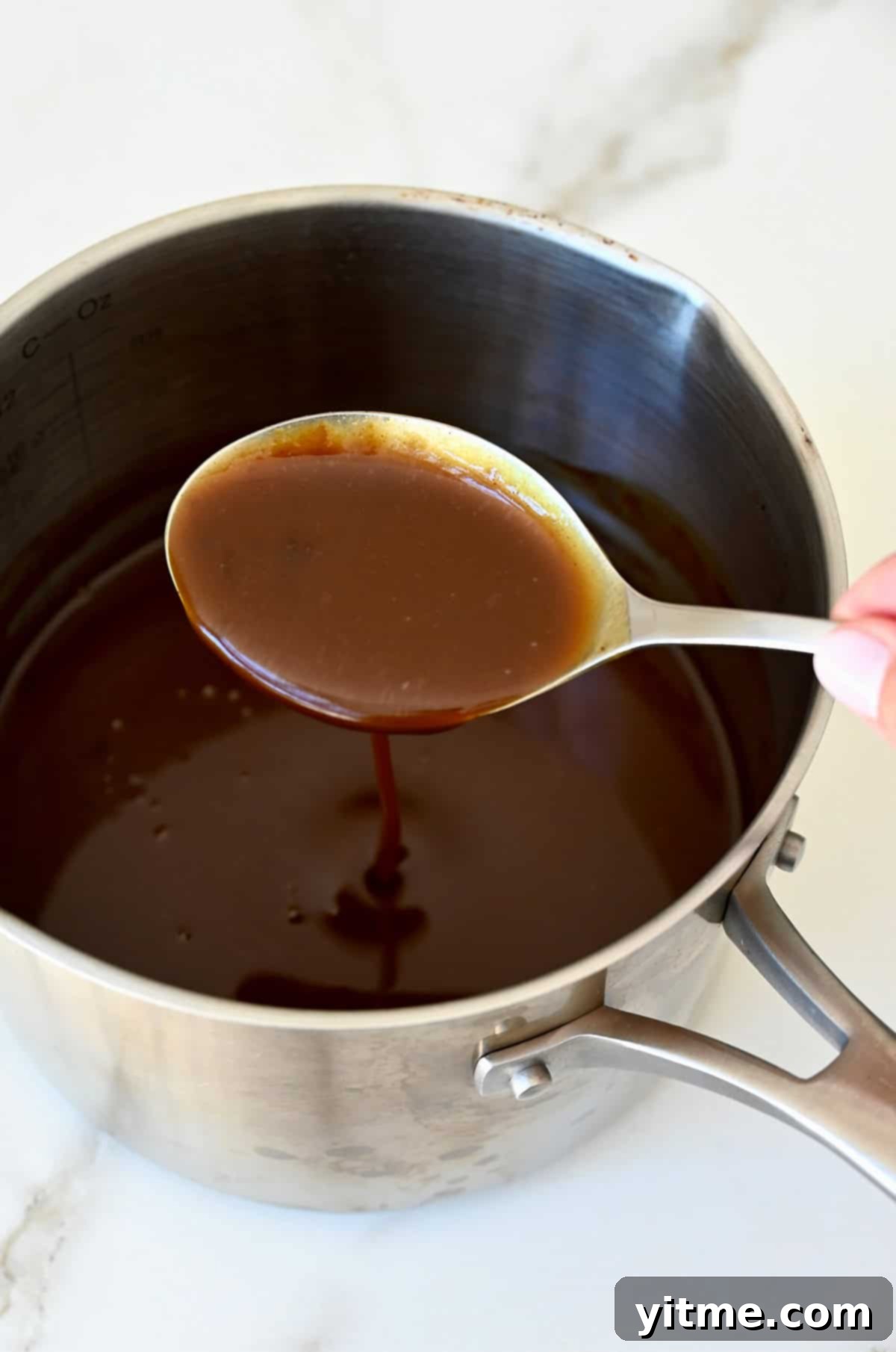 Balsamic Honey Pulled Pork: A Slow Cooker Delight 7 Thickened balsamic honey sauce covering a spoon that's above a saucepan.