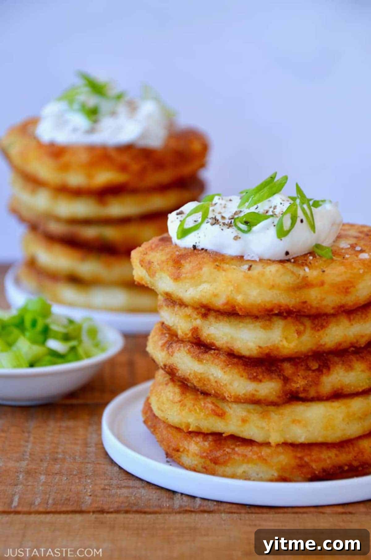 Mashed Potato Makeovers 3 A tempting stack of golden brown cheesy mashed potato pancakes, generously topped with a dollop of creamy sour cream and a sprinkle of fresh chopped scallions, inviting diners to enjoy.