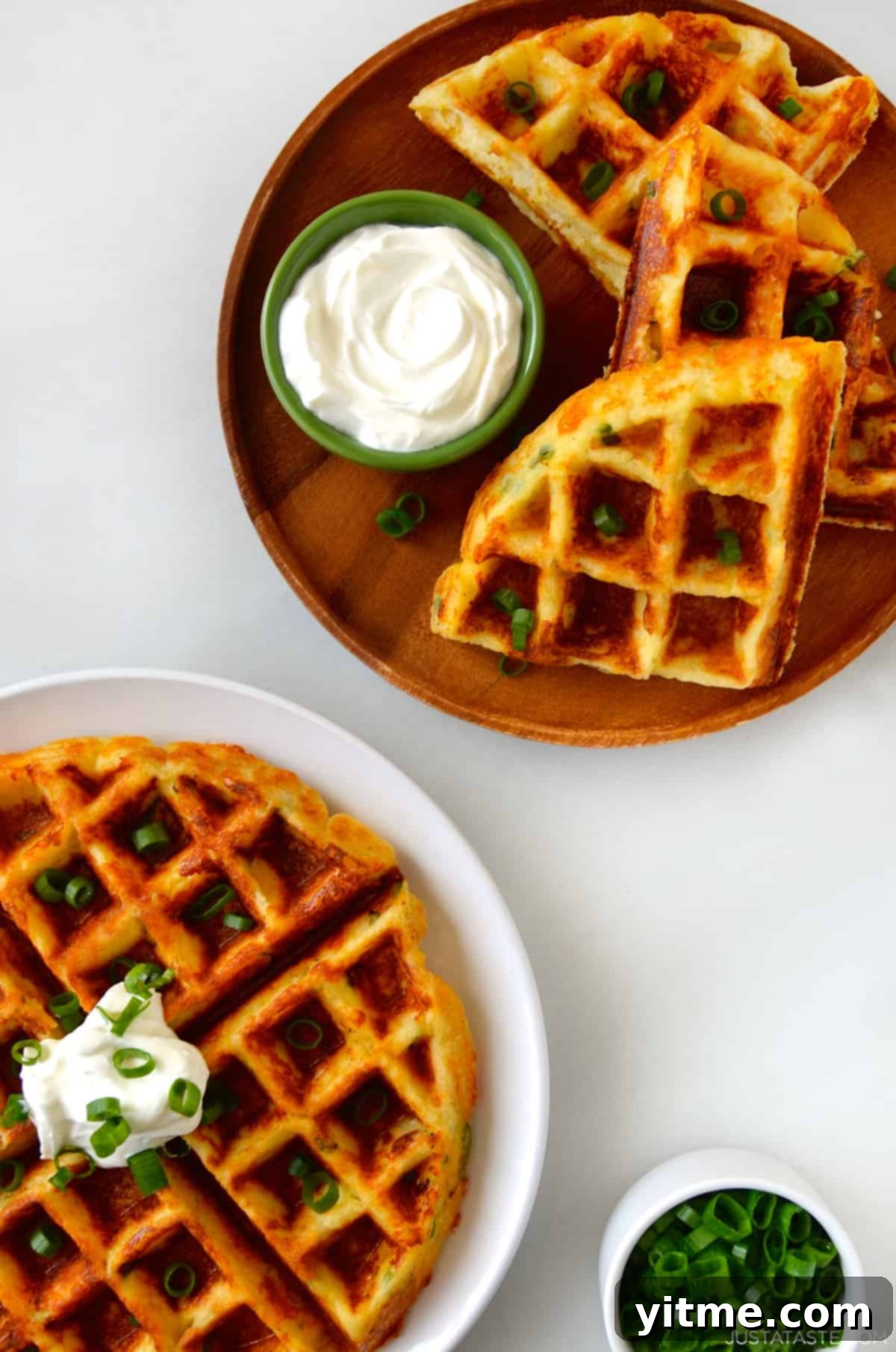 Mashed Potato Makeovers 6 Two plates each featuring a golden, crispy cheesy mashed potato waffle, generously topped with a dollop of creamy sour cream, showcasing their fluffy interior and crunchy exterior.