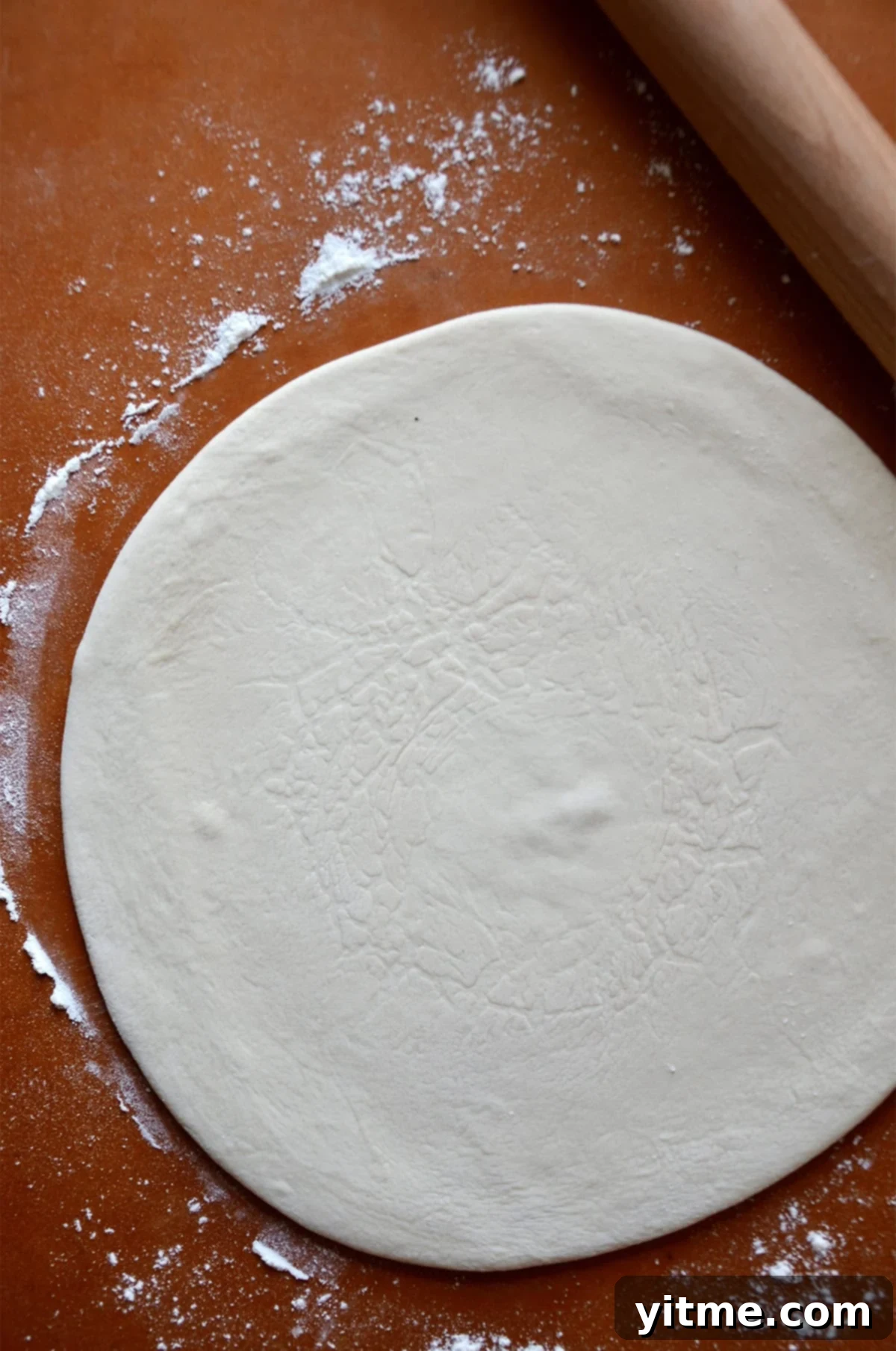 Garlic-Kissed Kale & Bacon Pie 3 A round of pizza dough on a floured surface with a rolling pin beside it.