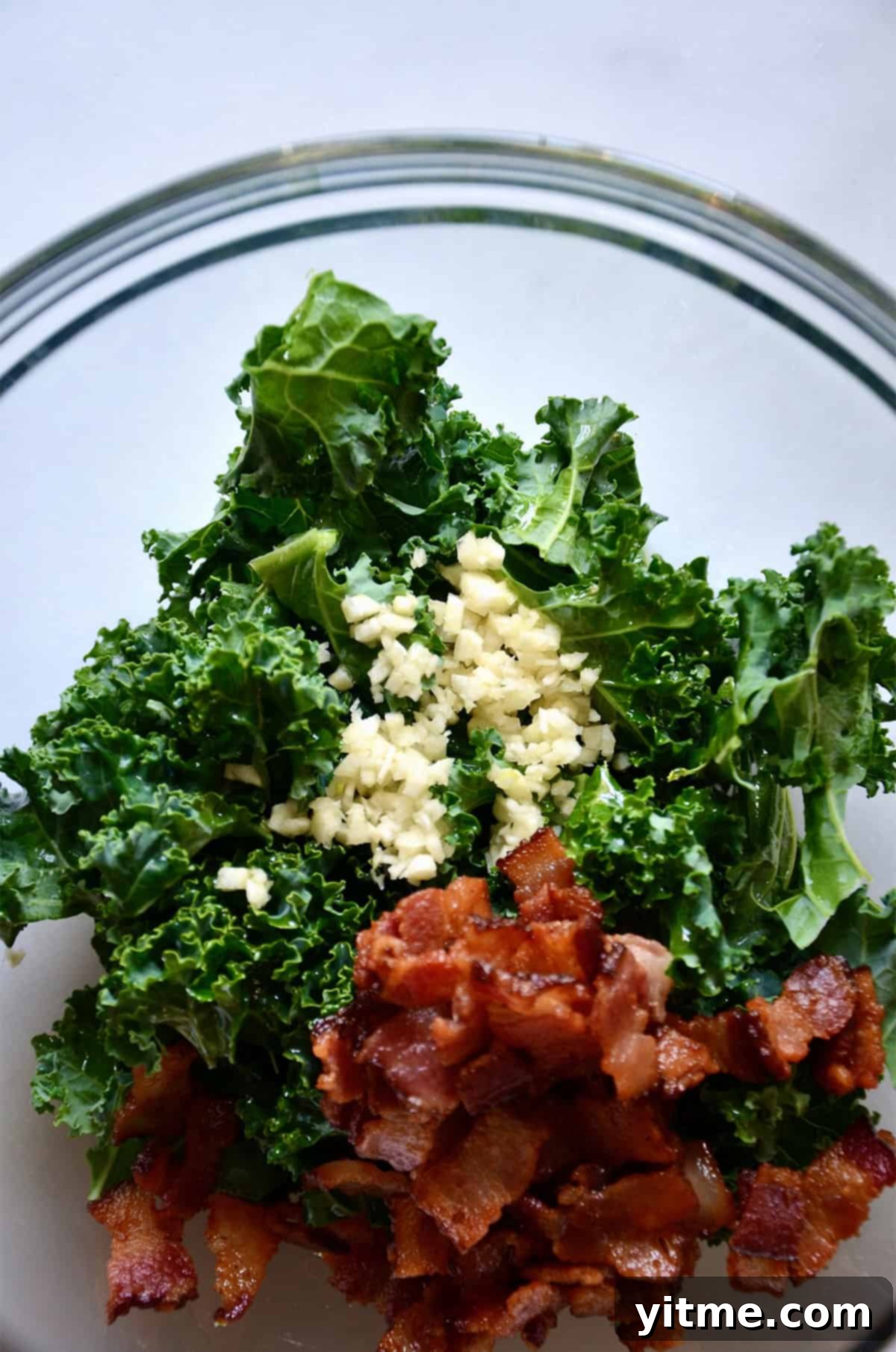 Garlic-Kissed Kale & Bacon Pie 4 Chopped kale, crispy pieces of bacon and minced garlic in a large glass bowl.