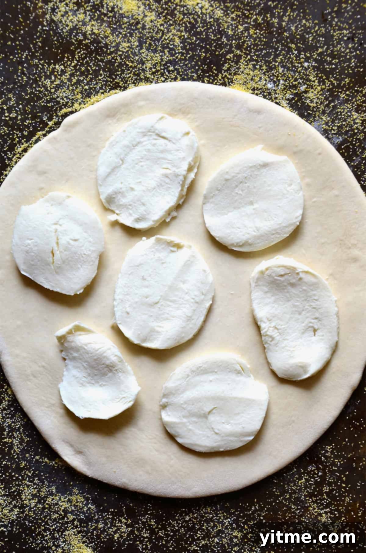 Garlic-Kissed Kale & Bacon Pie 5 Slices of fresh mozzarella atop pizza dough on a corn flour dusted surface.