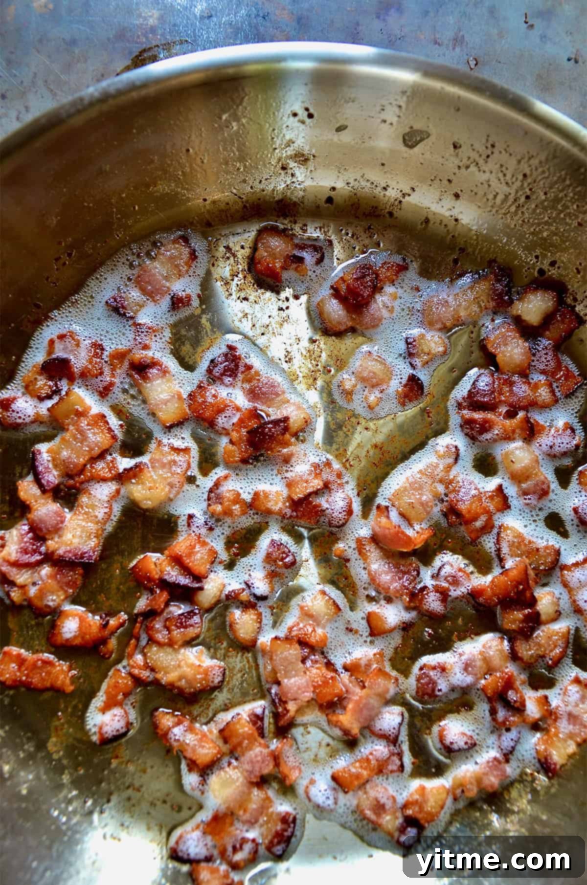 Pieces of bacon crisping in a stainless steel skillet
