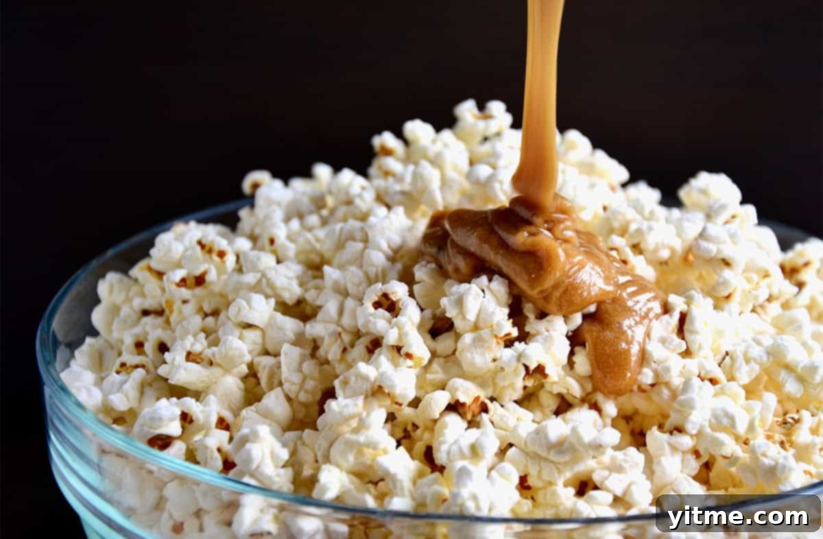 Caramel sauce being poured onto popcorn in a large glass mixing bowl