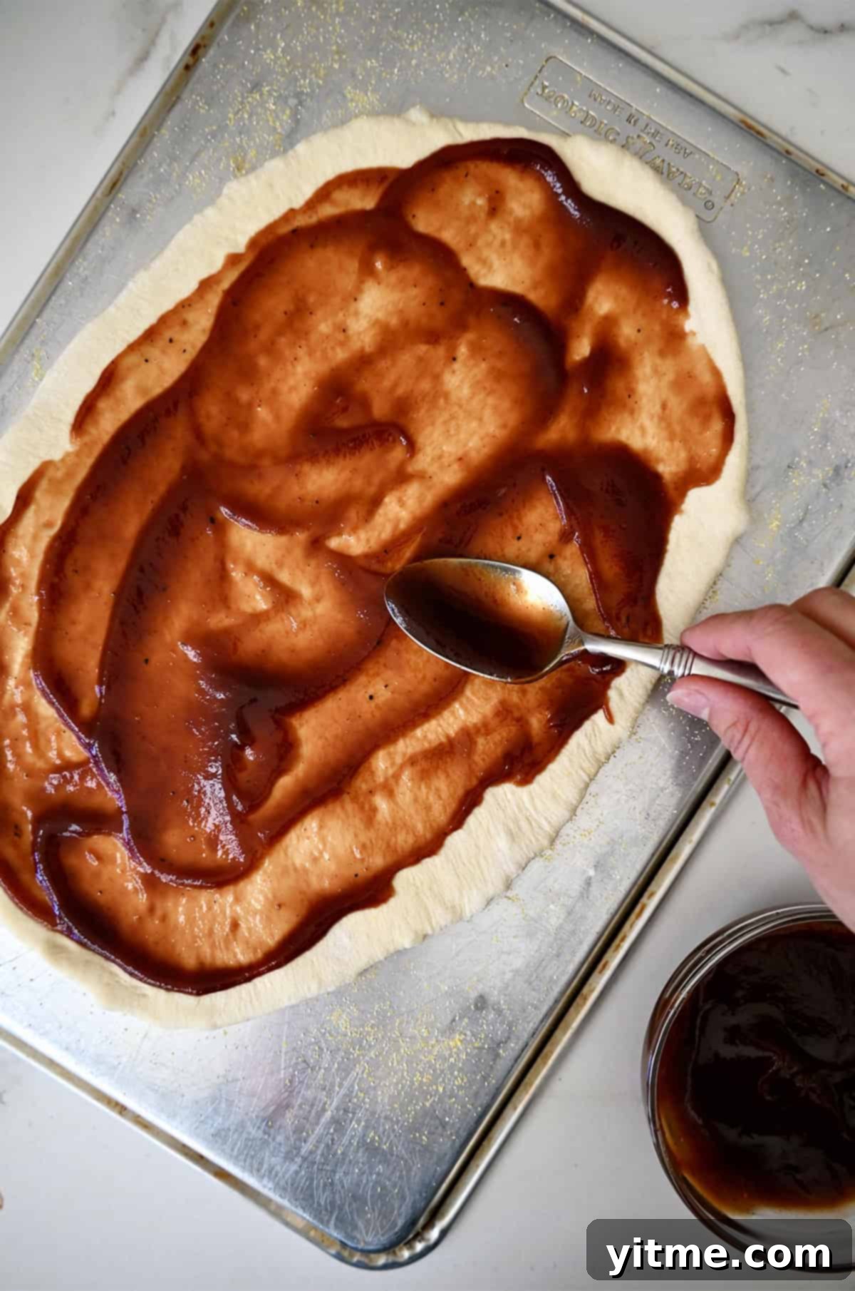 Spreading barbecue sauce on pizza dough.