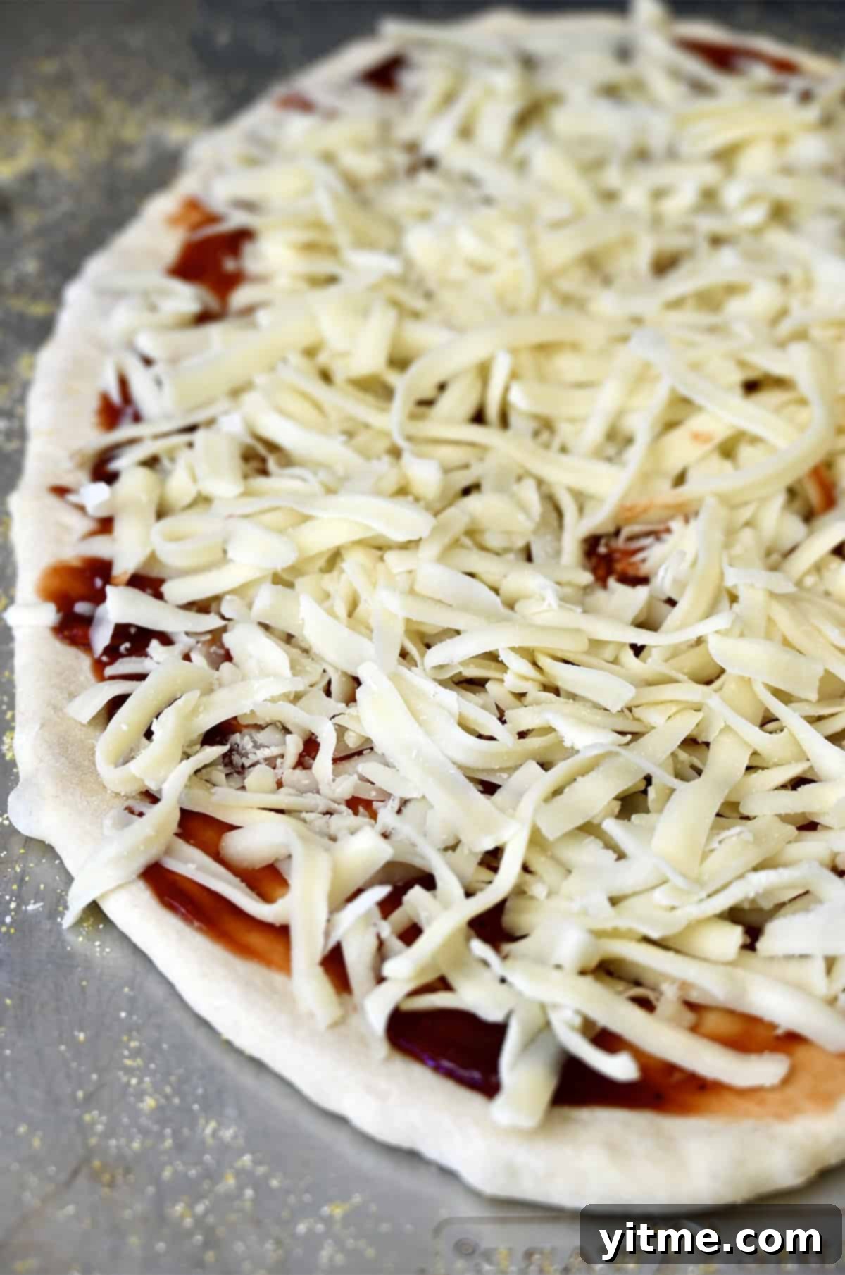 Shredded mozzarella atop barbecue sauce and pizza dough.