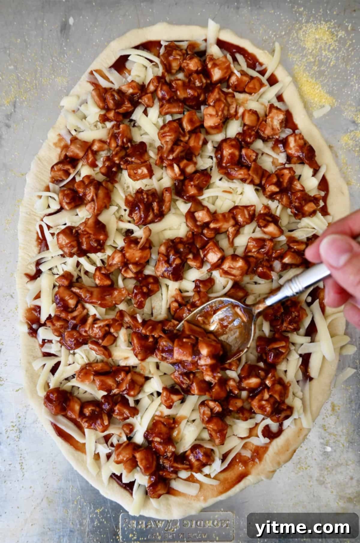 Adding barbecue-coated diced chicken atop mozzarella.