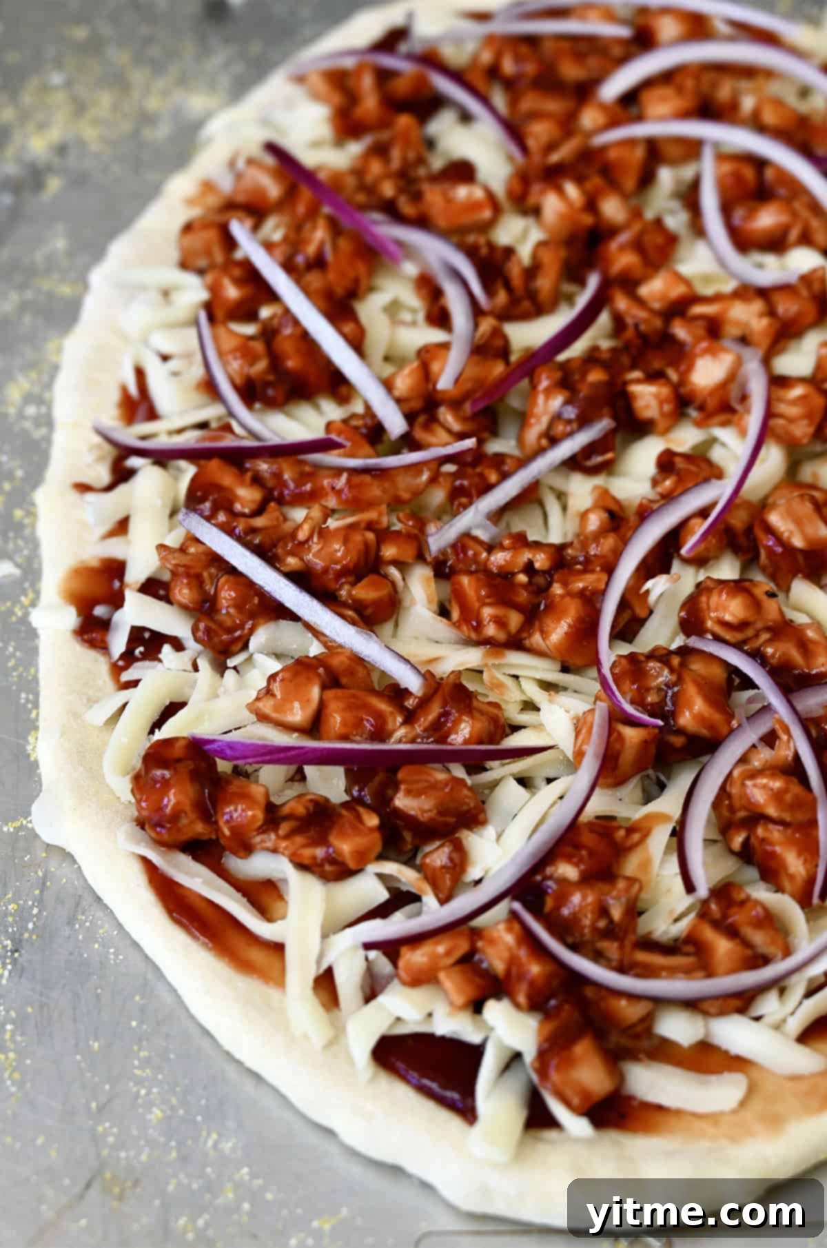 Pizza dough topped with barbecue sauce, mozzarella cheese, diced chicken, and red onions.