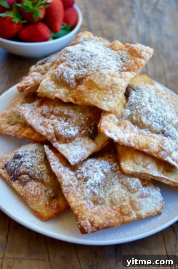 A plate of golden brown chocolate wontons generously dusted with powdered sugar, creating a visually appealing and delicious dessert.