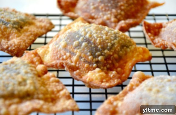 A wire cooling rack filled with freshly fried chocolate wontons, slightly cooled and ready for a dusting of powdered sugar.