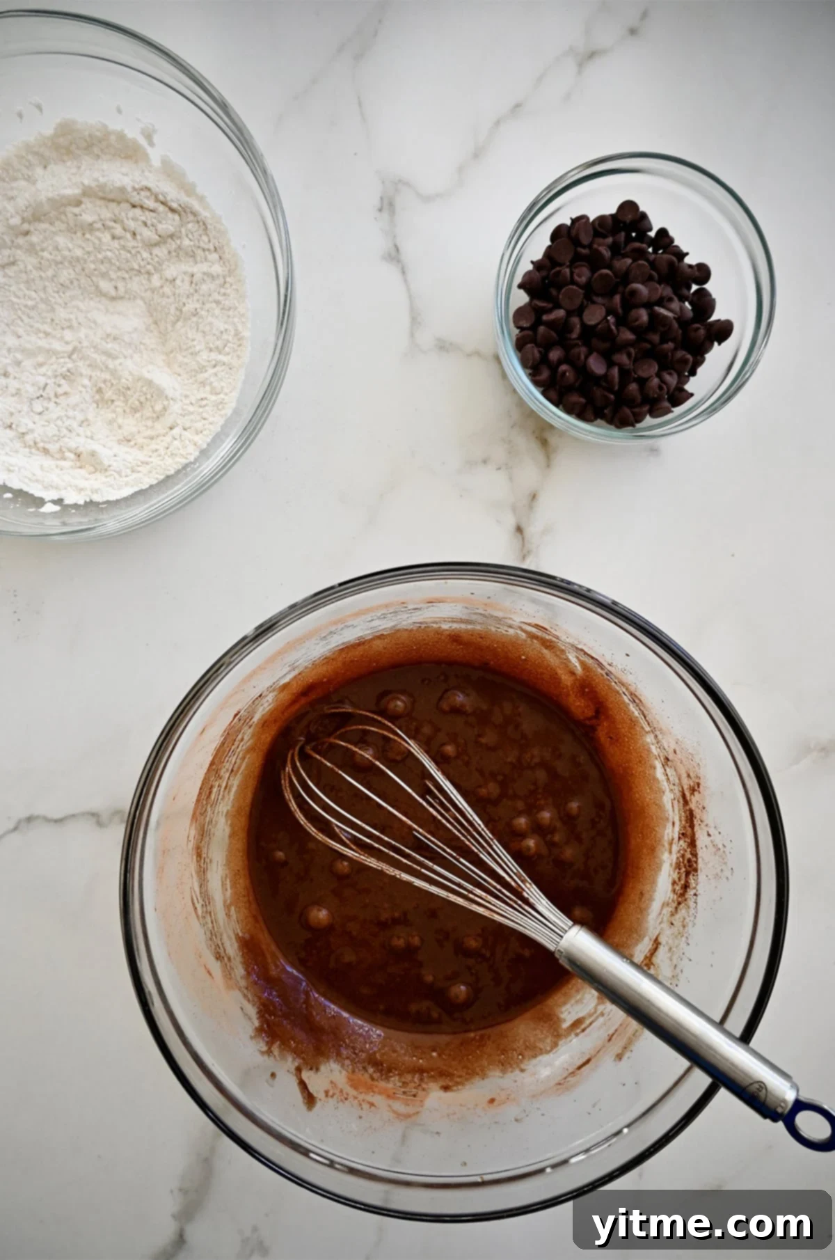 Fudgy Chocolate Brownie Shards 4 Three glass bowls displaying the separate stages of brownie bark preparation: dry flour mixture, smooth brownie batter with a whisk, and a bowl of chocolate chips.