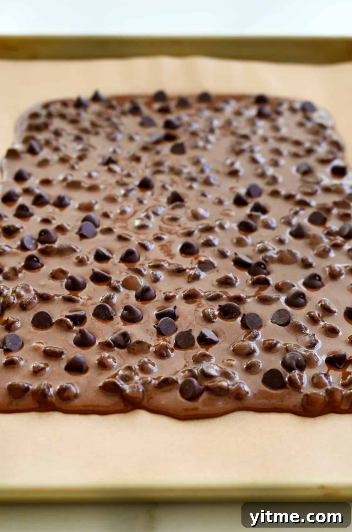 Fudgy Chocolate Brownie Shards 5 Smoothly spread brownie batter across parchment paper on a baking sheet, ready for baking.