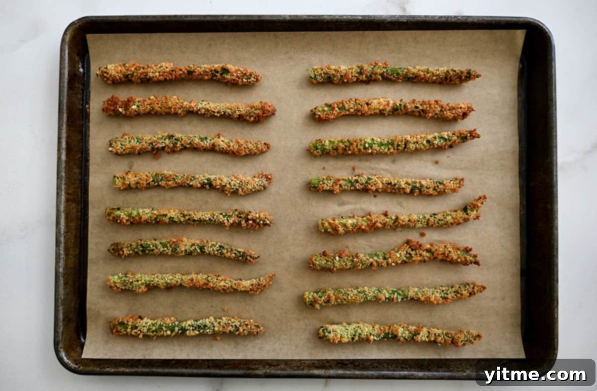 Rows of baked asparagus fries on a parchment-lined baking sheet.