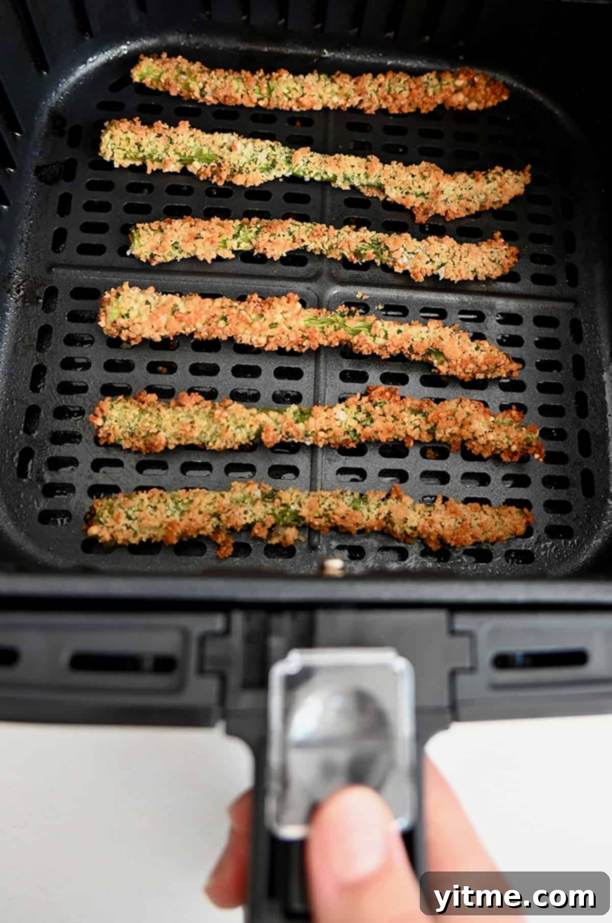 Baked asparagus fries lined up in an air fryer basket.