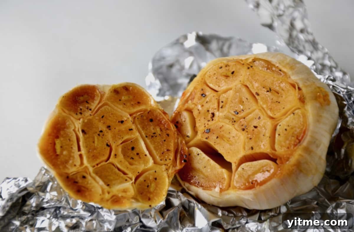 A head of roasted garlic sliced in half and wrapped in aluminum foil.