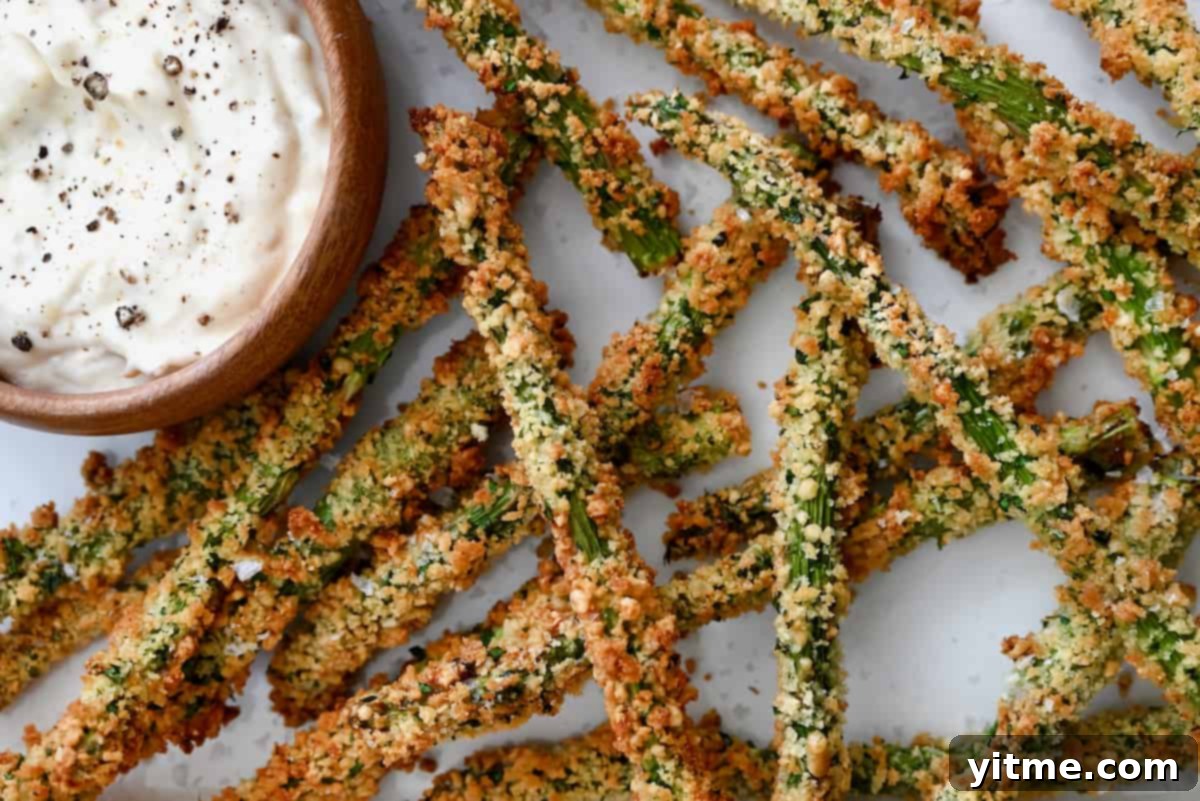 Baked asparagus fries piled on a white surface with roasted garlic aioli.