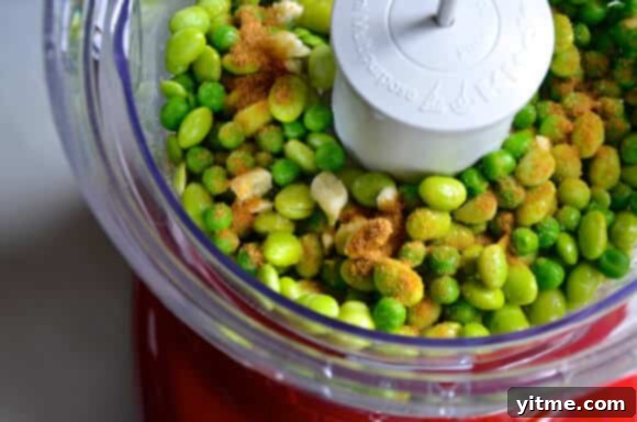 Close-up of a serving of creamy edamame and pea hummus in a white bowl with a spoon.