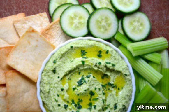 Overhead shot of creamy edamame and pea hummus in a bowl, surrounded by fresh ingredients like lemon and parsley.