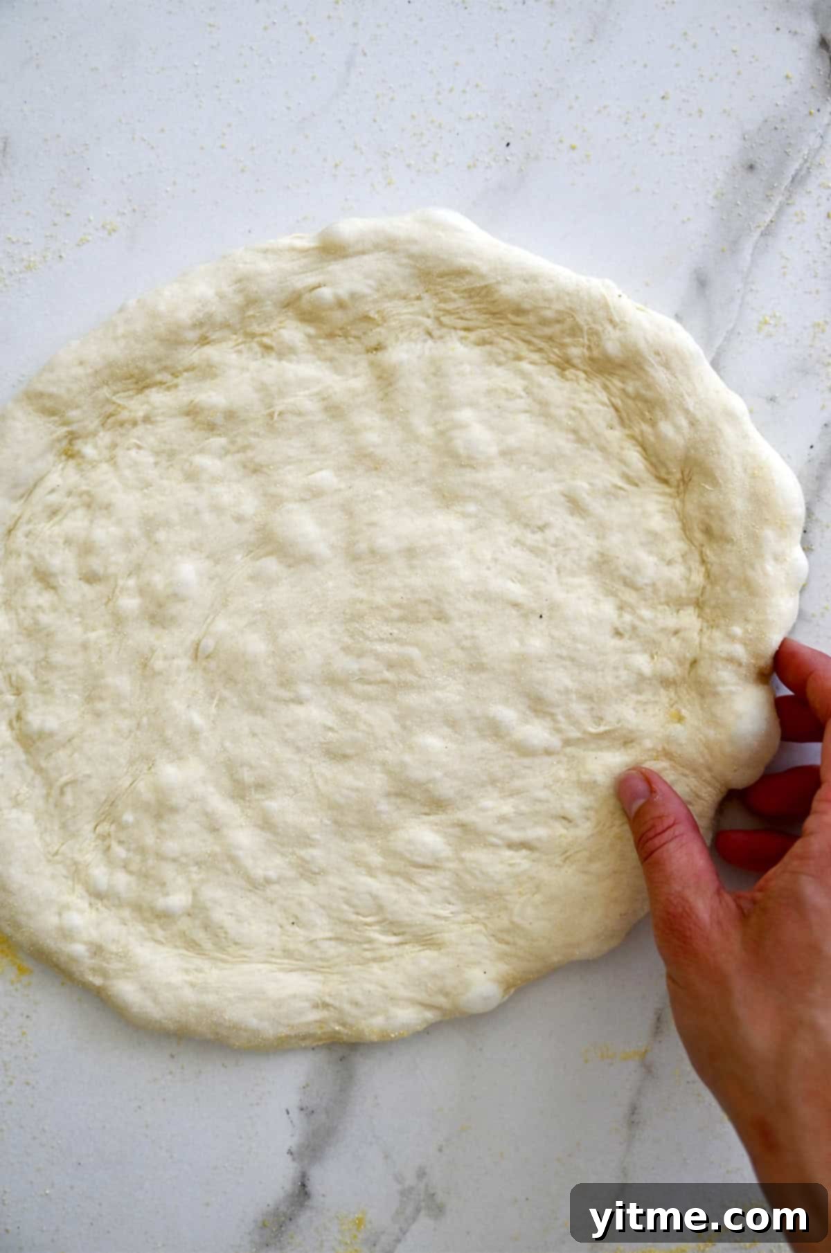 Pizza dough shaped into a circle with a hand holding onto it.