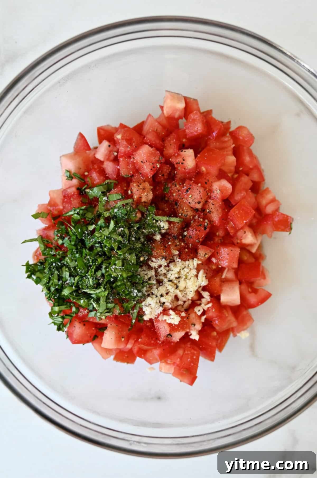 Diced tomatoes, minced garlic, chopped fresh basil and olive oil in a glass bowl.