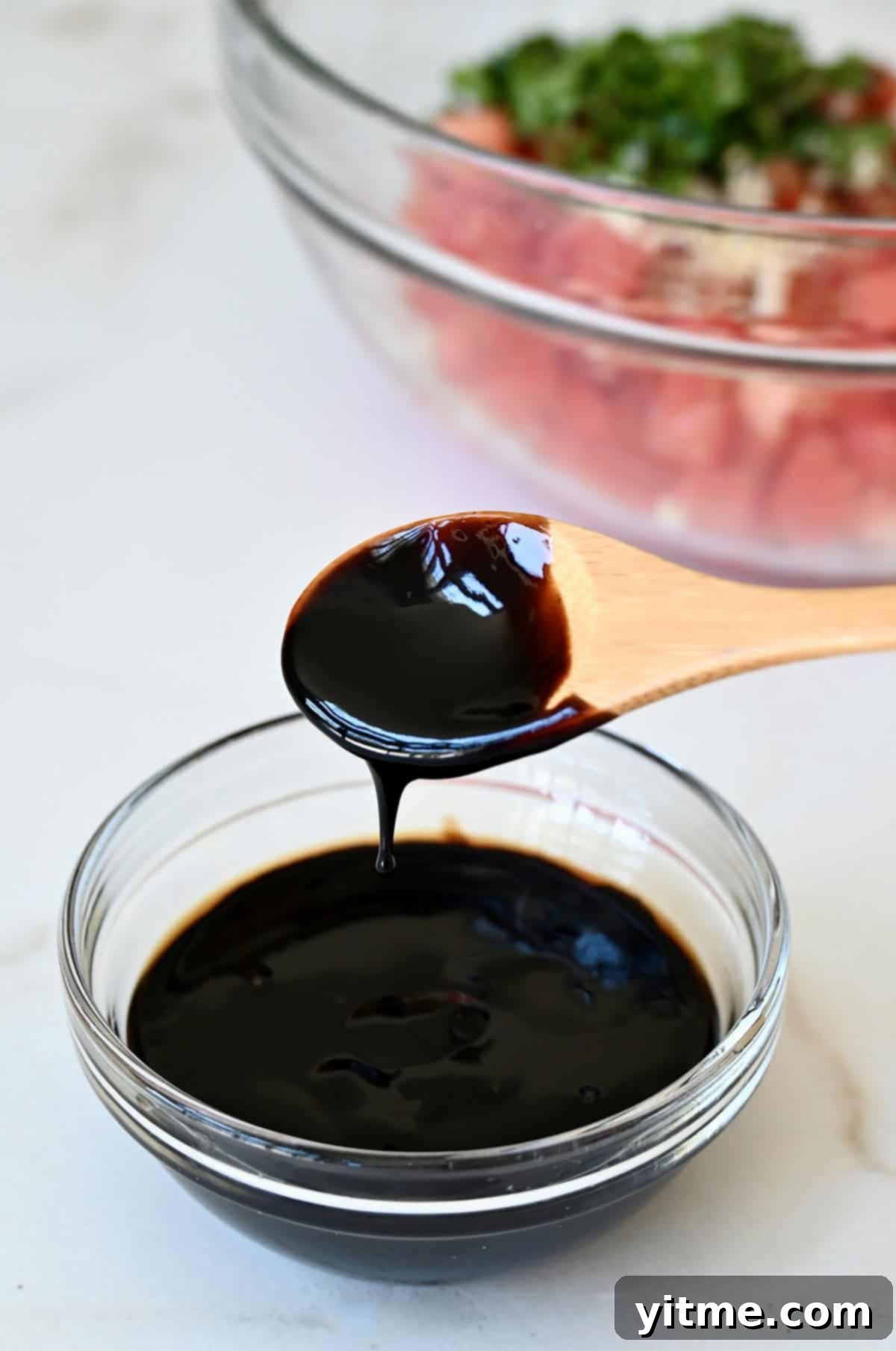 A spoon covered in balsamic reduction over a small glass bowl.