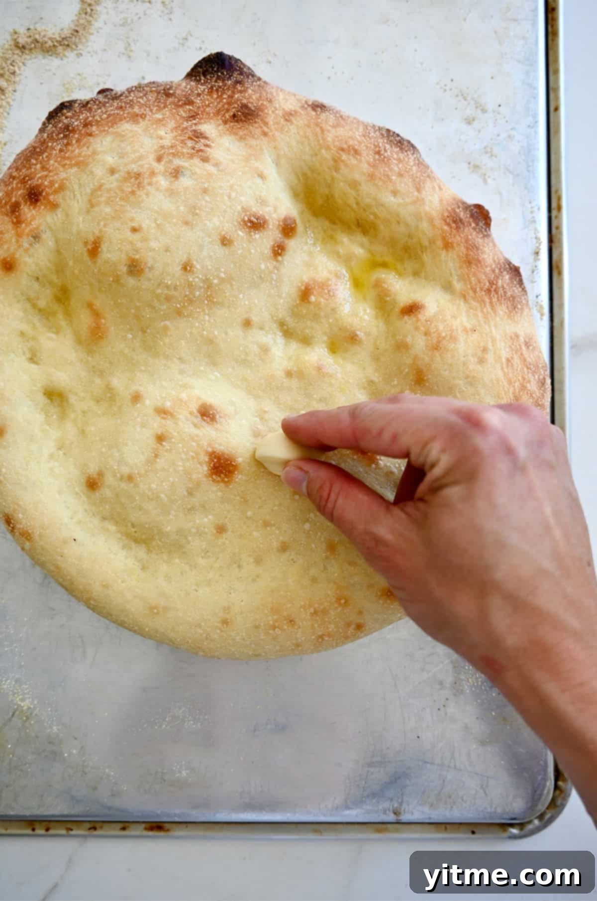 A hand holding a raw garlic clove rubs it atop hot pizza crust fresh out of the oven.