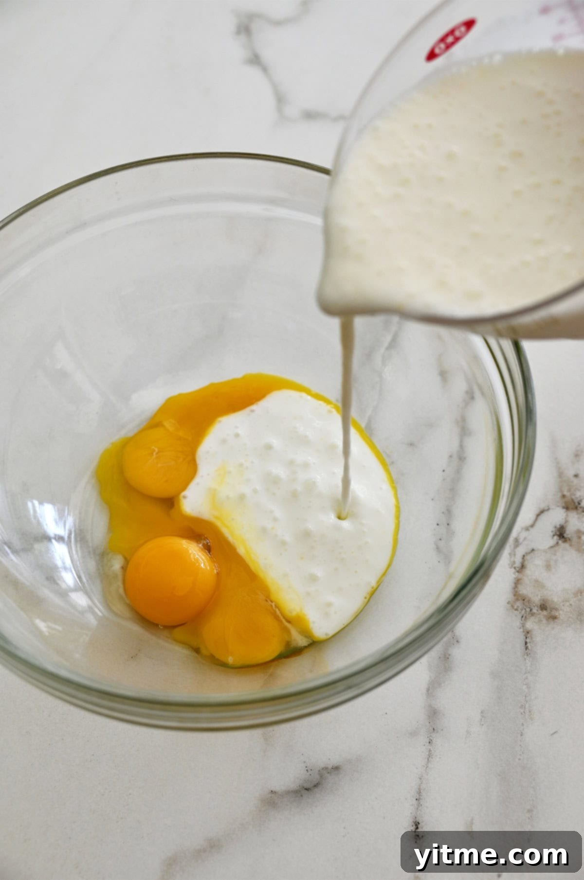 Golden Belgian Waffles From Scratch 4 Buttermilk being poured from a liquid measuring cup into a bowl with three egg yolks.