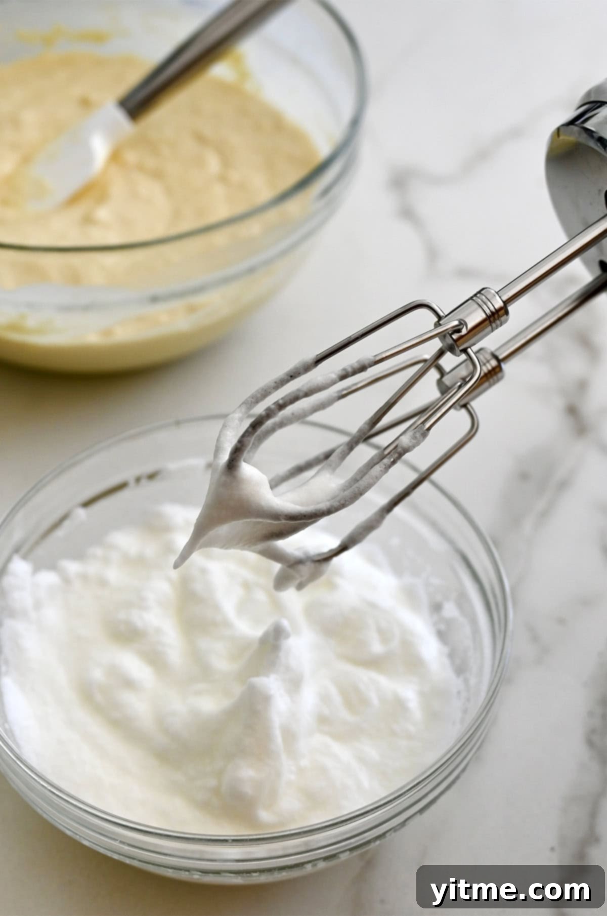 Golden Belgian Waffles From Scratch 7 An electric mixer hovers over a bowl containing whipped egg whites.