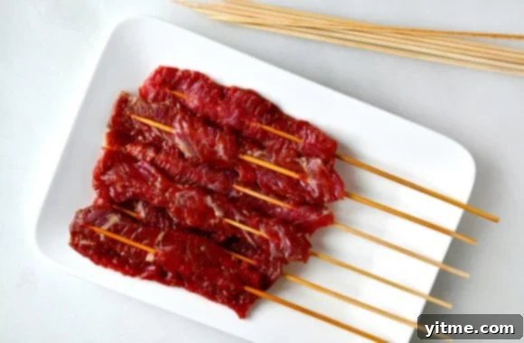 Five-Spice Beef Skewers 3 A white plate containing marinated beef kabobs on wooden skewers