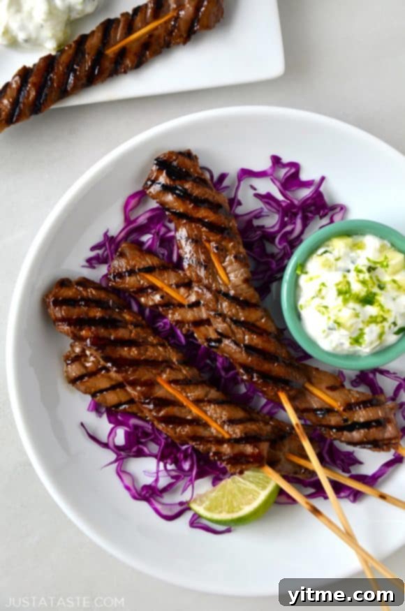 Five-Spice Beef Skewers 2 A circular white plate with purple cabbage, beef skewers, and yogurt dip