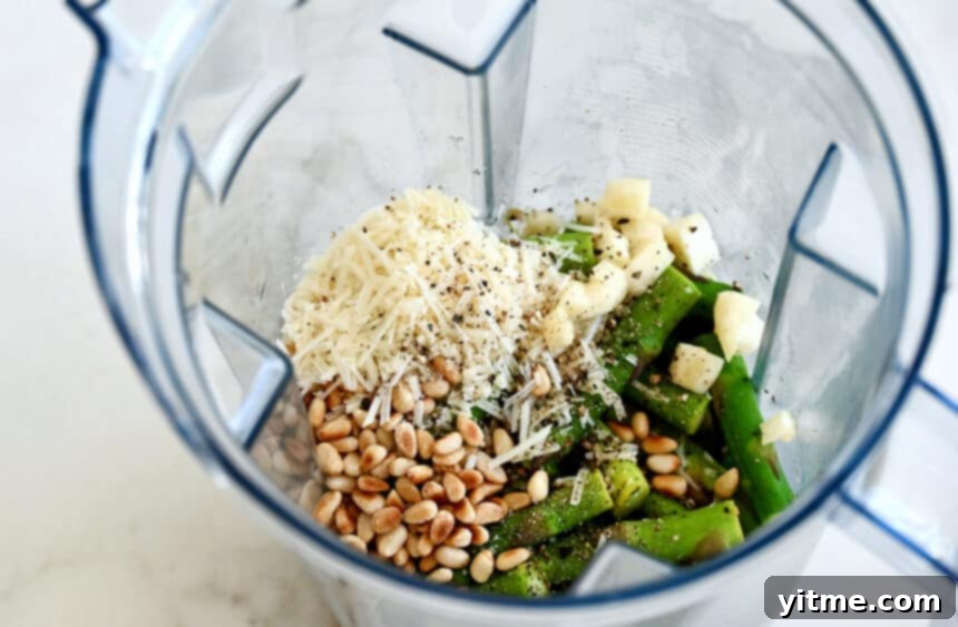 Creamy Asparagus Pesto Pasta 4 A top-down view of a blender containing toasted pine nuts, shredded Parmesan cheese, garlic cloves, salt and pepper, waiting for the blanched asparagus and olive oil.