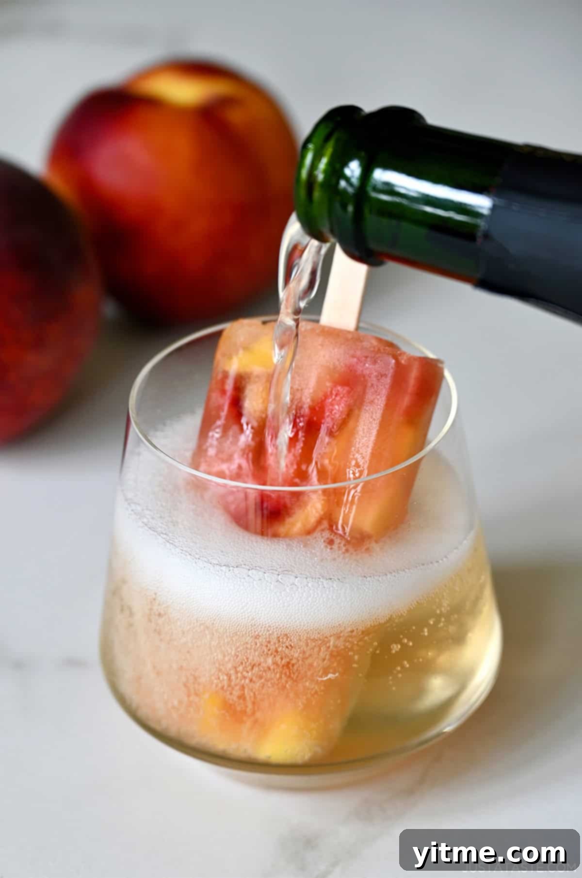 A Peach Sangria Popsicle elegantly served in a wine glass, topped with bubbly Prosecco, creating a sophisticated cocktail-slushie hybrid.