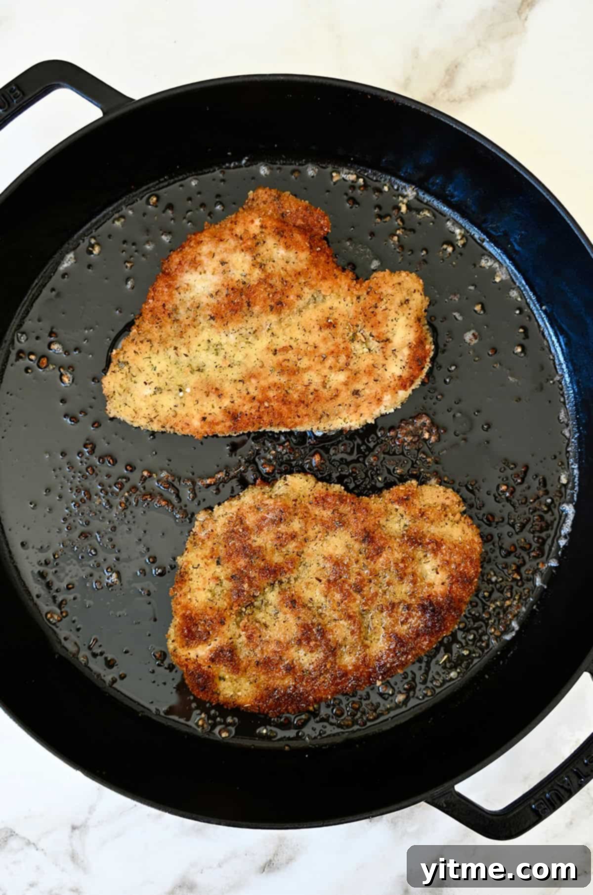Pan-fried chicken cutlets in a skillet for Chicken Milanese