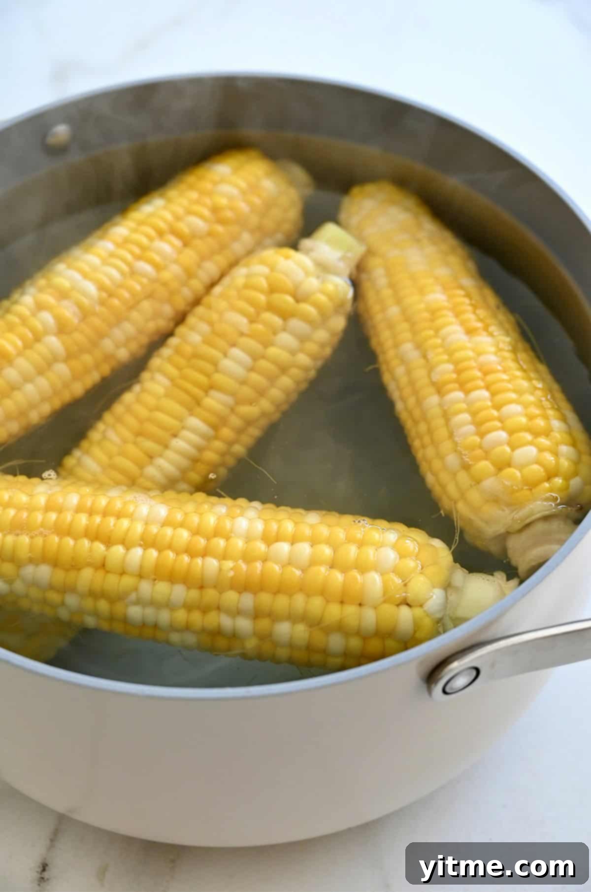 Four ears of corn are gently boiling in a large pot of water, ready for preparation into delicious Mexican street corn.