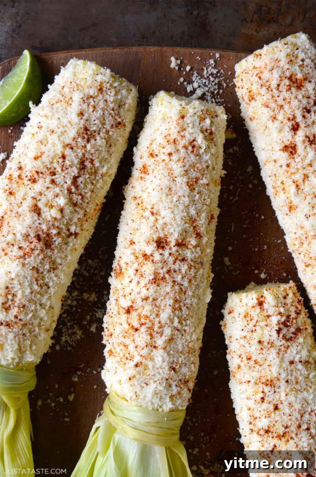 A perfectly prepared ear of Mexican street corn (elote) slathered in creamy sauce, coated in crumbled Cotija cheese, and generously sprinkled with vibrant chili powder, ready to be enjoyed.