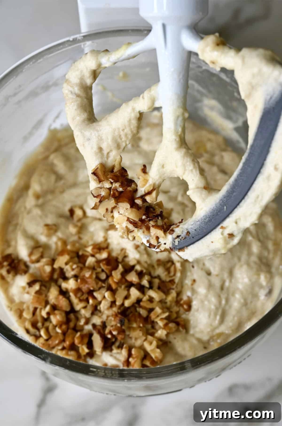 Banana cake batter topped with walnuts in the bowl of a stand mixer.