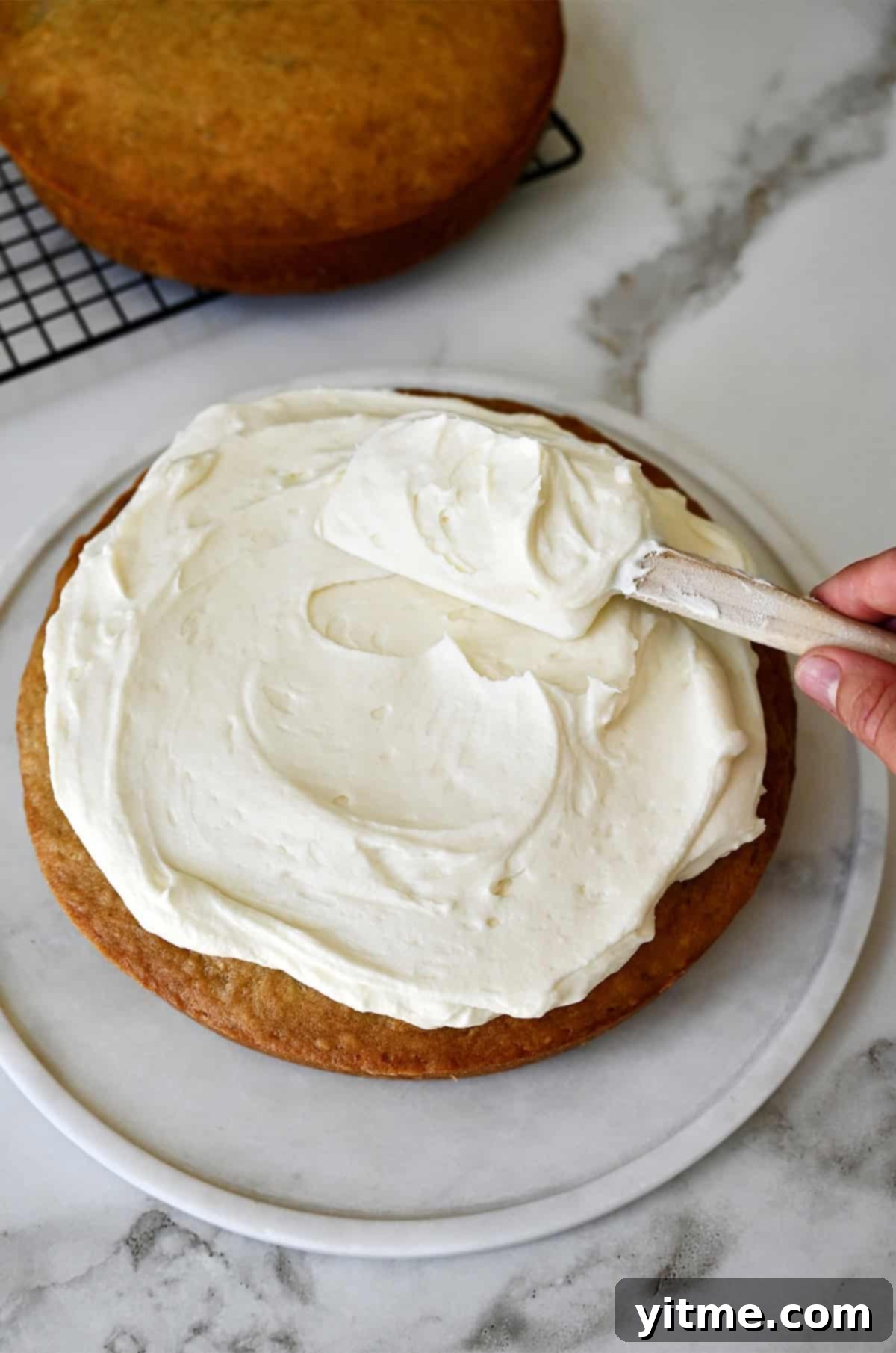 Cream cheese frosting being spread atop a round banana layer cake.